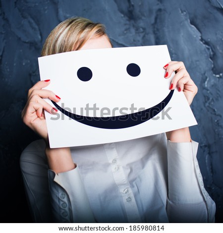 Young woman holding a cardboard with a smiley face on it in front of her head. Photo in color style instagram filters