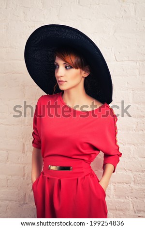 Beautiful young fashionable woman posing in red dress and black hat. Vogue style