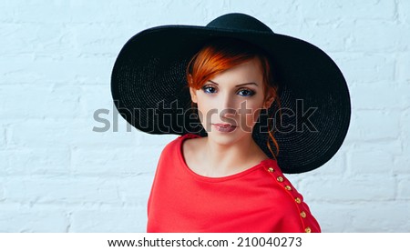 Beautiful young fashionable woman posing in red dress and black hat. Vogue style.