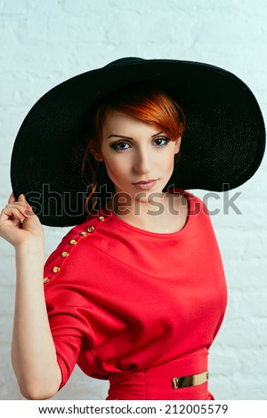 Beautiful young fashionable woman posing in red dress and black hat. Vogue style