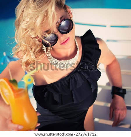Fashion beautiful woman sunbathing on a chaise lounge with fresh orange juice in luxury pool. Vogue style. Photo with instagram style filters