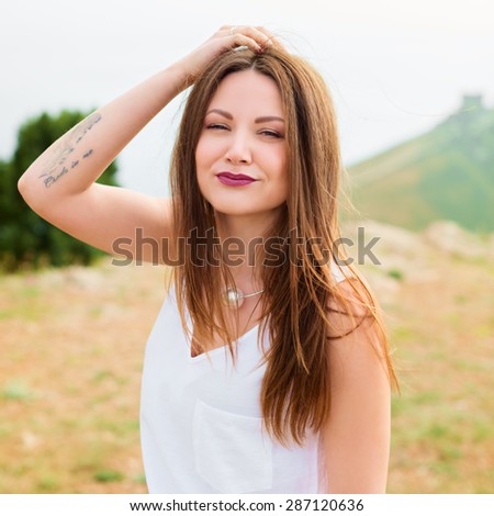 Smiling girl enjoys fine warm spring weather highly in mountains against the sea. Beautiful modern woman with long hair in a white shirt outdoors. Photo with instagram style filters