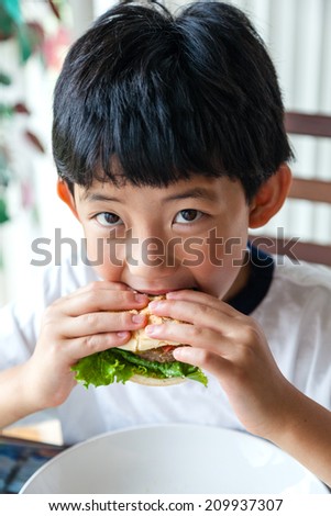 Asian boy taking a bite on his burger.