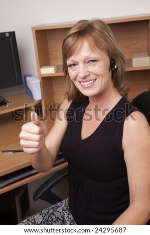 A business woman giving a thumbs up sign at her office desk