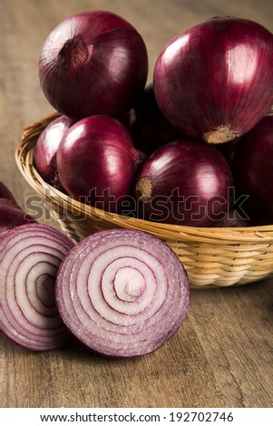 A close-up of red onions in a basket and a cut red onion over a table.