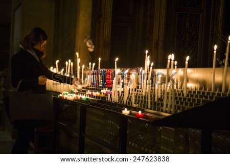 Woman lighting prayer candle aka offering, sacrificial or memorial candles lit in a church. Sacre Coeur.