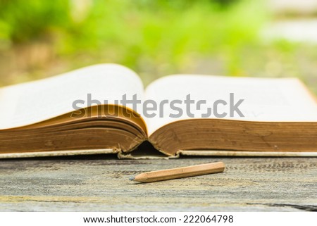 Concept wood pencil on wooden table with old book in garden.
