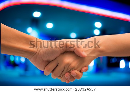 Business man and woman make hand shake with abstract bokeh light of petrol station.