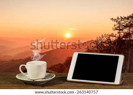 Hot coffee with tablet PC on table. With natural sunrise with mountain background.