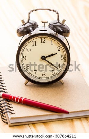 alarm clock on book and pen on office table.