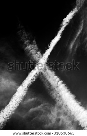 X shape created in the sky by passing by planes with some other clouds, makes a great nature background. Black and white photo.