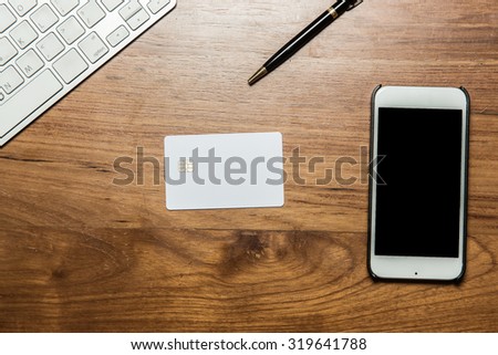 Keyboard, credit card, pen and smartphone on wooden office table. Top view.