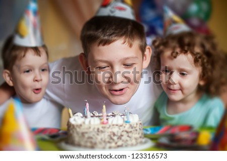 boy blows out the candles on a birthday cake and hugs his brother and sister