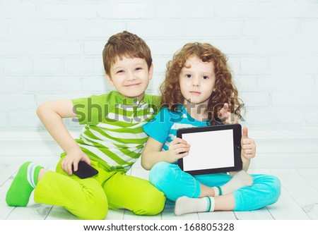 Twins boy and girls with the tablet PC on a light background. Holding thumbs up.