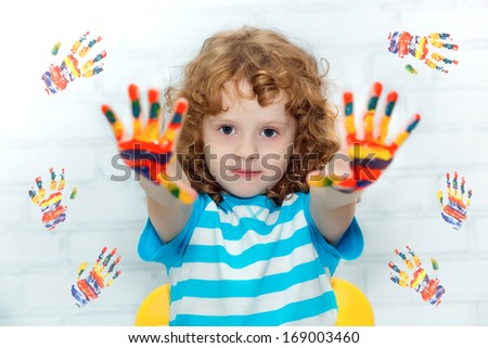 Funny little curly girl with hands in the paint. On a light background with colored prints of paint.