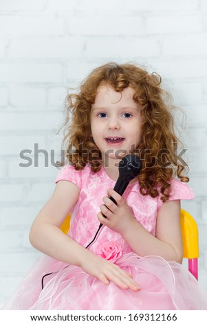 Little girl in a pink dress, singing with microphone in studio on light background.