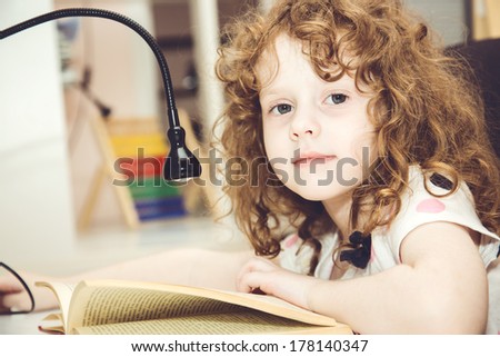 Beautiful curly-haired girl reading a book at his desk.