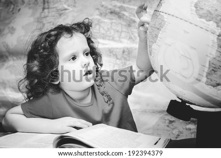 Black and white portrait of a little girl looks at the globe.