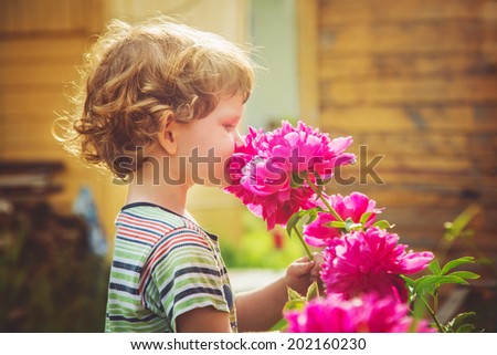 Child smelling bouquet of peonies, sun back lighting. Toning photo. Vintage instagram filter.