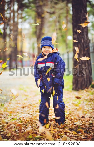 Happy little boy throws the autumn leaves in the air.