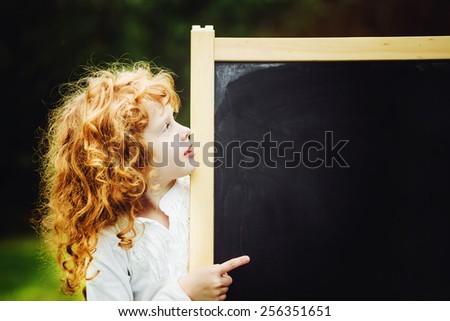 Little girl pointing finger at blackboard. Educational concept. Place for your information or advertisement.