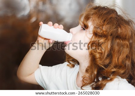 Little girl is drinking for milk or yogurt from bottles. Portrait view profile.