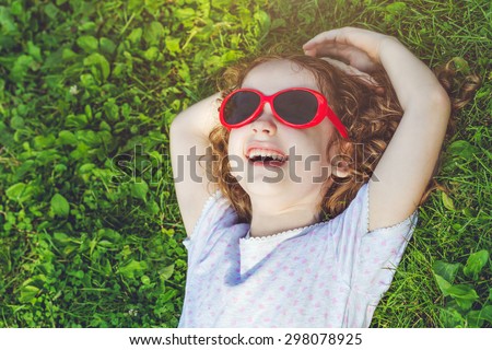 laughing girl with glasses lying on the grass in a summer park. Happy childhood concept. Background toned in instagram filter.