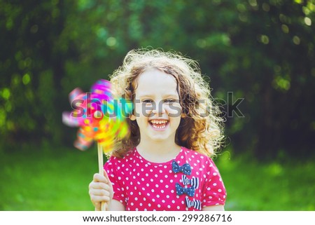 Little girl with rainbow pinwheel toy in summer park. Eco, travel, vacation, family concept.