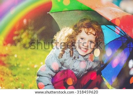 Laughing girl in the rain with a rainbow and with color bokeh.  Happy and healthy childhood concept.