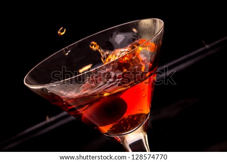 Red splashing cocktail glass with cherry in black ambient light.