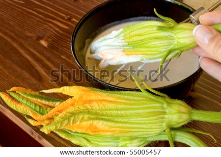 Food And Drinks - Italian Food - Fried zucchini flowers preparation - Closeup of hand passing a zucchini flower in the batter.