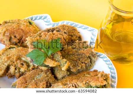 Food Recipes - First courses - Italian fried artichokes and jar with olive oil isolated on yellow background.