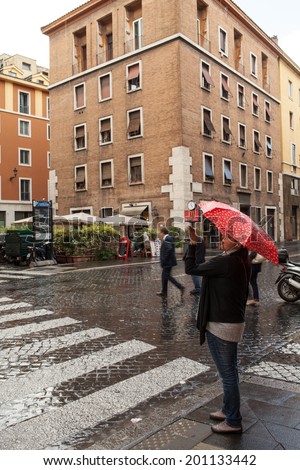 ROME, ITALY - JUNE 18, 2014: Tourist with red umbrella taking shots of Rome under the rain with the smartphone.The rain has hit Rome for the fourth consecutive day in June.