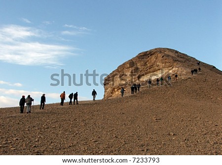 Group of people hiking in the desert to the top of  mountain, blue sky with clouds in the background