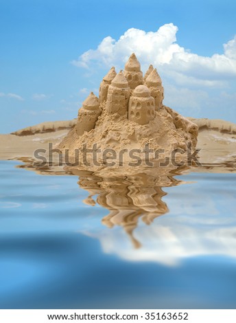 Sand castle on blue sky background with reflection on water