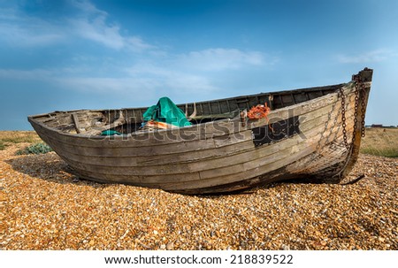 Old wooden boat washed up on a shingle beach under a sunny blue sky