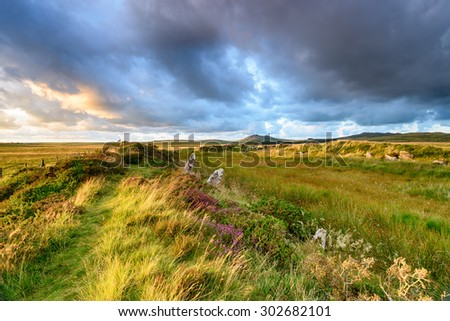 Dramatic sunset sky over King Arthur\'s Hall, a Neolithic monument made up of standing stones in a remote part of Bodmin Moor in Cornwall, with the peaks of Roughtor and Brown Willy in the distance