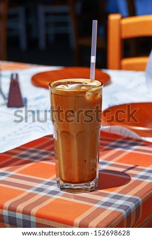 Glass of ice cold frappe coffee with a drinking straw on an outdoor cafe table