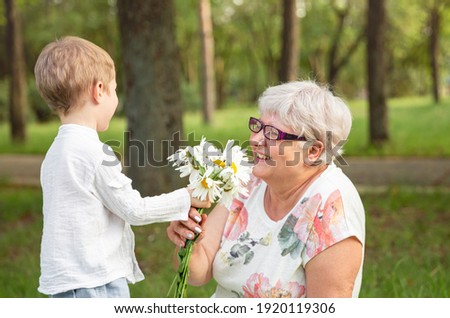 Beautiful boy giving a flower to grandma. Happy mothers day. Grandson and grandmother spending time together. Act of kindness to an elderly woman. Funny boy with flowers and his grandmother in park. 商業照片 © 