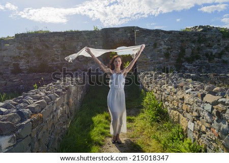 Beautiful brunette woman in white dress posing at Ancient wall of ruined city. Freedom and lifestyle concept. Outdoor portrait of a young woman. Series