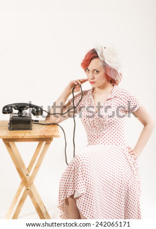 Fashion young redhead woman with a retro look waiting by the phone, isolated on white