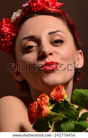 Fashion portrait of a redhead woman with flowers in hair holding orange roses . Attractive redhead woman. Close up portrait. Studio shot