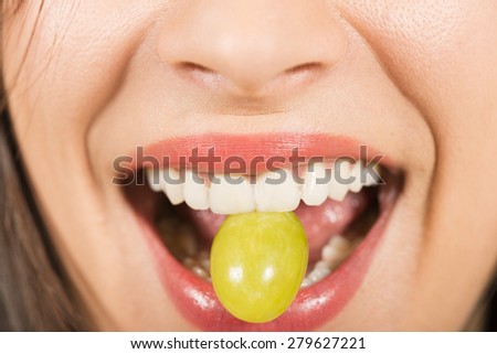 Close up of a woman mouth biting white grape, studio shot on white background