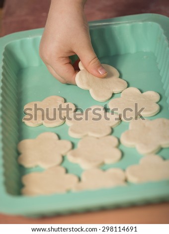 Little chef hands smeary with flour, putting the dough cut in flower shaped, in the baking tray