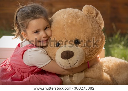 Outdoor portrait of expressive little girl hugging huge plush bear. Little girl playing with teddy bear
