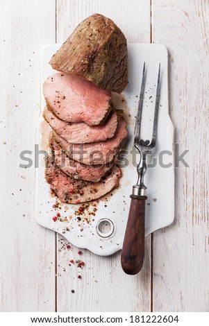 Roast beef and meat fork on white wooden background