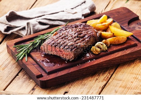 Sliced medium rare grilled Beef steak Ribeye with roasted potato wedges on cutting board on wooden background