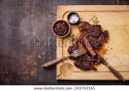Sliced medium rare grilled Beef steak Ribeye with salt and pepper on meat cutting board on dark wooden background