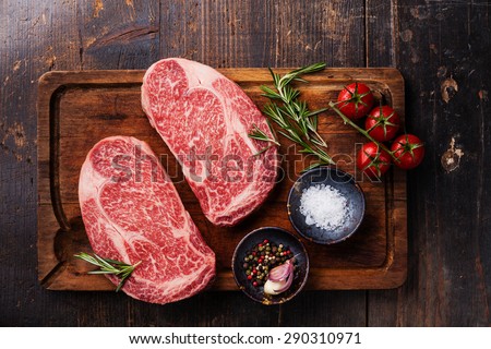 Two Raw fresh marbled meat Black Angus Steak Ribeye and seasonings on dark wooden background