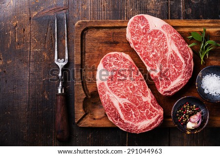 Two Raw fresh marbled meat Black Angus Steak Ribeye, seasonings and meat fork on dark wooden background